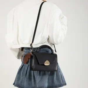 Minimalist black leather handbag with gold drop lock shown from side on model