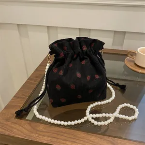 Sac seau en velours noir à motif fraise avec bandoulière perles sur table