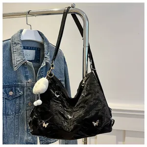 Close-up of black pleated tote bag with silver butterfly charms and white fur ball keychain