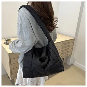 Detail of a large black quilted puffer tote bag with wide shoulder straps on a model