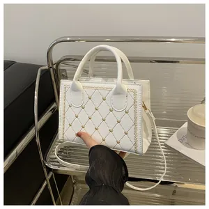 Détail du sac blanc matelassé avec broderie coeur doré sur un support métallique