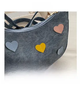 Detailed macro view of denim crescent bag featuring colorful leather heart patches and gold zipper