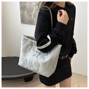 Detail of silver metallic tote bag featuring pleated texture and metal butterfly bow charm