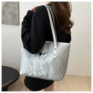 Detail of silver metallic tote bag with crinkled texture and butterfly badge detail