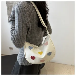 Detail of white crescent hobo bag with colorful heart patches worn on the shoulder