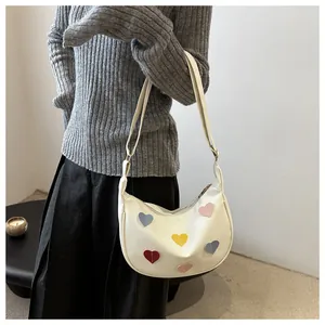 Close-up of a white crescent shoulder bag with colorful heart-shaped stitched patches