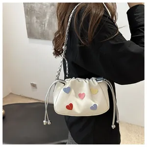 Close-up of a white canvas bucket bag featuring colorful heart patches and silver chain strap