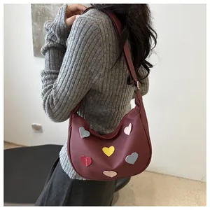 Model wearing a burgundy crescent bag with colorful heart patches and fabric strap