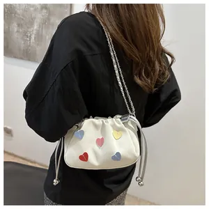 Detail of white drawstring bucket bag featuring multi-color leather heart patches and chain strap