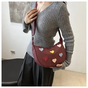 Detail of burgundy crescent shoulder bag with colorful heart patches on grey knit top