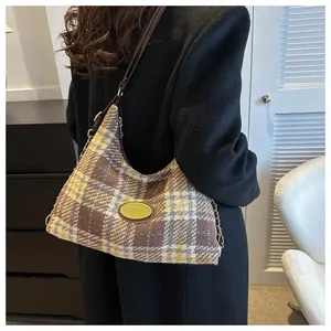 Détail d'un sac à bandoulière en tweed à carreaux avec lanière en cuir sur un manteau noir