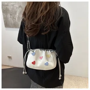 Detail of white drawstring bucket bag with colorful stitched heart patches and silver chain
