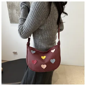 Detail shot of burgundy crescent shoulder bag with colorful heart patches on model