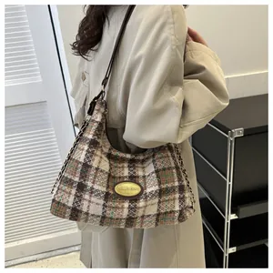 Gros plan du sac hobo en tweed avec plaque logo dorée et bandoulière en cuir et chaîne