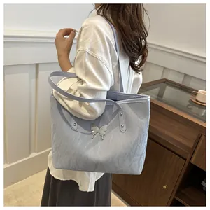 Detail view of light blue tote bag with metallic butterfly emblem and wrinkled texture