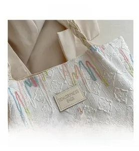 Detail of white tote bag with pastel chain embroidery and braided woven handle strap