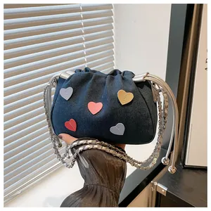 Detail of blue denim bucket bag with colorful heart patches and silver metal chain strap