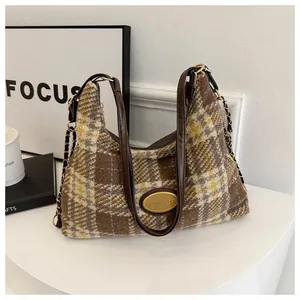 Détail de la texture en laine à carreaux marron et du logo métallique doré sur le sac