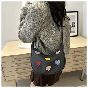 Detail of black crescent shoulder bag with colorful heart patches on minimal interior background