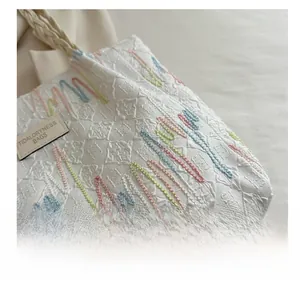 Detail of white tote bag featuring diamond texture and colorful embroidered wave lines
