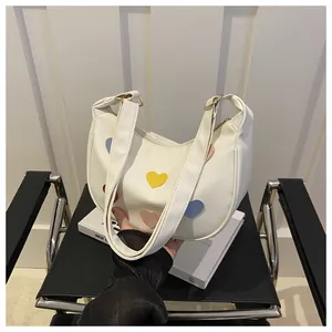 Detail view of white crescent shoulder bag with colorful heart patches and gold buckles