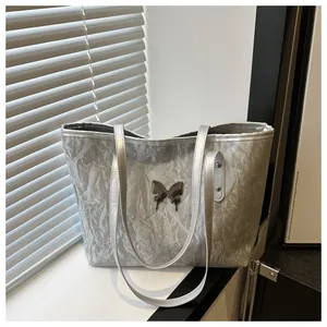 Detailed view of the silver metallic tote bag with wrinkled texture and butterfly charm