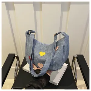 Detail of blue denim crescent bag featuring colorful leather heart patches and strap