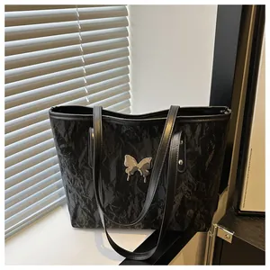 Close-up of black wrinkled texture tote bag featuring a silver metal butterfly ornament