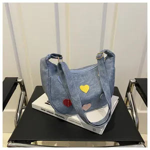Detail of blue denim crescent bag featuring colorful heart patches and adjustable strap