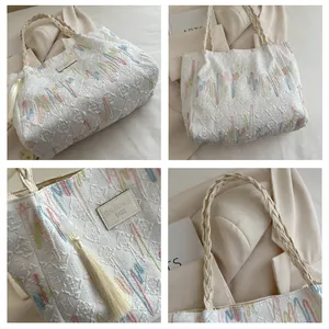 Detail of white tote bag with woven handles, embossed patterns, and tassel decoration