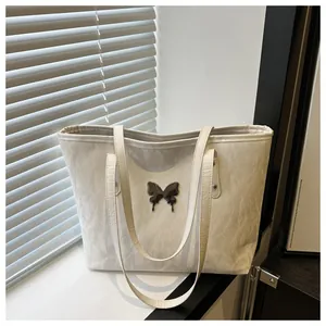 Detail of cream white tote bag featuring black butterfly charm and pleated leather texture