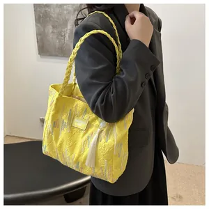 Detailed view of yellow tote bag with letter embossing, woven strap and white tassel
