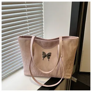 Detail of pink pleated tote bag featuring a metallic butterfly emblem on white surface