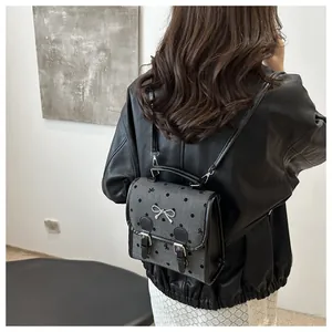Detail of grey polka dot mini backpack worn by model showing black leather straps and silver bow