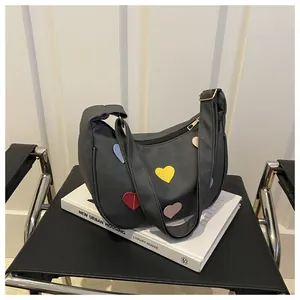 Detail of black crescent shoulder bag featuring colorful stitched heart patches and zipper