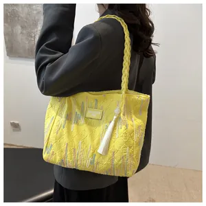 Detail view of yellow tote bag with letter embossing and white pearl tassel charm