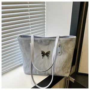 Close-up of light blue textured tote bag with silver liquid butterfly metal charm