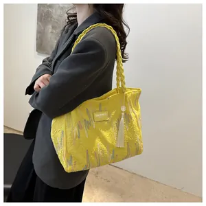 Detail of yellow tote bag with woven handles, fringe charm and embossed texture