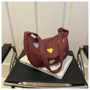 Detail of burgundy crescent shoulder bag with colorful heart patches on a sleek black chair