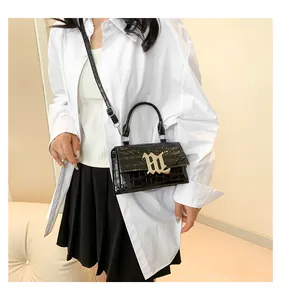Schwarze Handtasche mit Krokodilmuster und goldener M-Metallschnalle getragen am Model