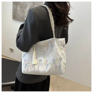 Detail of white tote bag featuring woven straps, colorful embroidery, and tassel accent