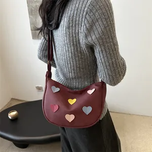 Chic burgundy crescent hobo bag with colorful heart patches on a grey sweater