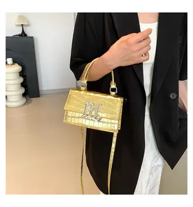 Detail einer goldenen Kroko-Handtasche mit silbernem M-Logo und elegantem Tragegriff