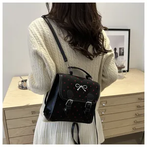 Detail of black mini backpack with red heart patterns and silver bow buckle on model