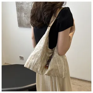 Detail of light beige tote bag featuring textured fabric and dark brown woven knot charm