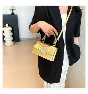 Goldene Handtasche mit Krokodilprägung und B-Logo getragen von Model im schwarzen Anzug