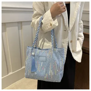 Detail of light blue tote bag featuring colorful wavy embroidery and woven handles