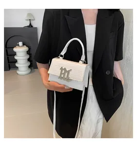 Detail der weißen Handtasche mit Krokodilprägung, großem Metallverschluss und Rundgriff