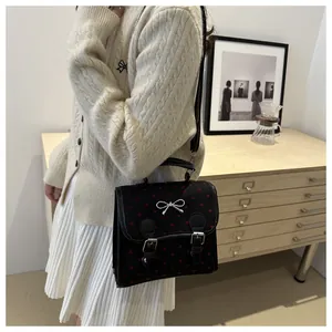 Chic black handbag with red hearts and silver bow detail worn in a cozy room setting