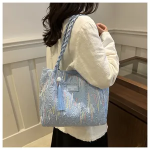 Detail of light blue quilted tote with wave embroidery and tassel on braided handle